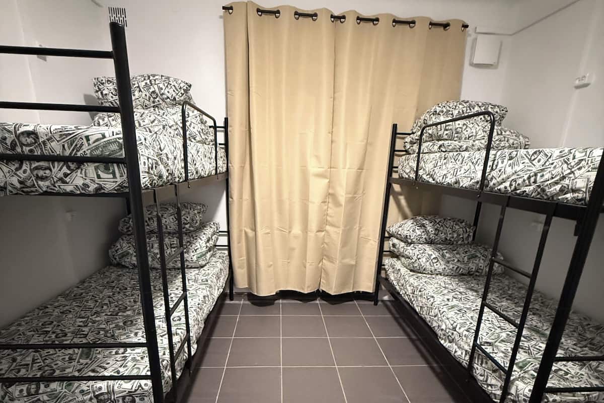 A dormitory room with bunk beds, a curtain, and tiled flooring.