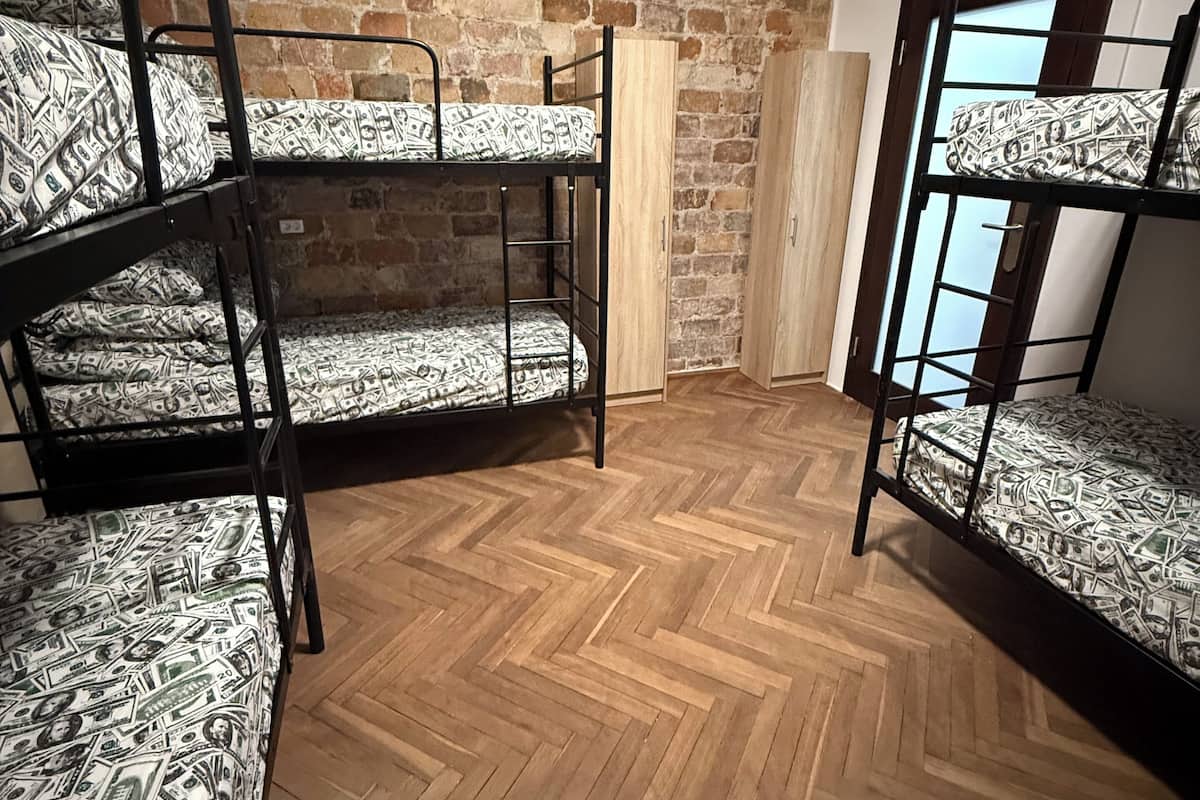 A room with three bunk beds, a wooden herringbone floor, a brick wall, and a window with a view.