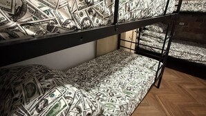 A bunk bed with mattresses covered in dollar bill patterns, wooden flooring, and a brick wall in the background. - HOSTEL PULSE (Warsaw)