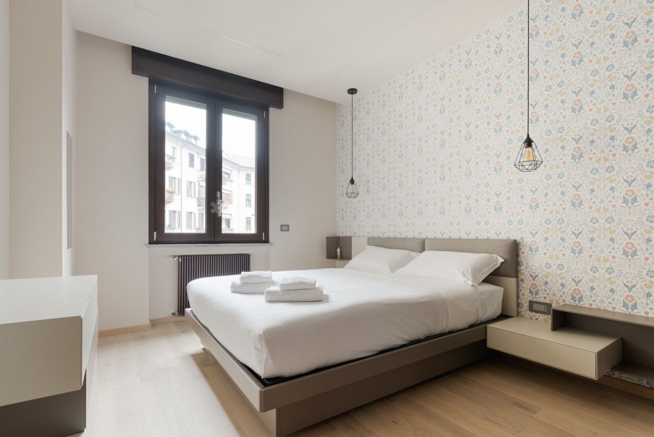 A modern bedroom with a bed, bedside tables, a window, and patterned wallpaper.
