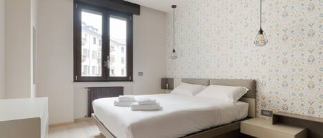 A modern bedroom with a bed, bedside tables, a window, and patterned wallpaper.