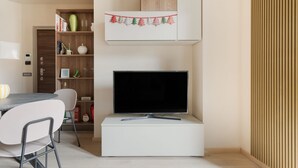 Ett modernt vardagsrum med en platt-TV, ett matbord med stolar, en bokhylla och en dekorativ julgransgirland.
