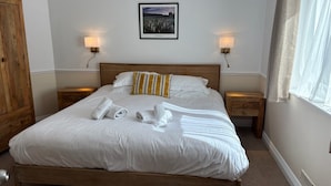 A neatly made bed with white linens, two bedside lamps, a framed picture on the wall, and a wooden wardrobe. - Byways Apartments (Salisbury)
