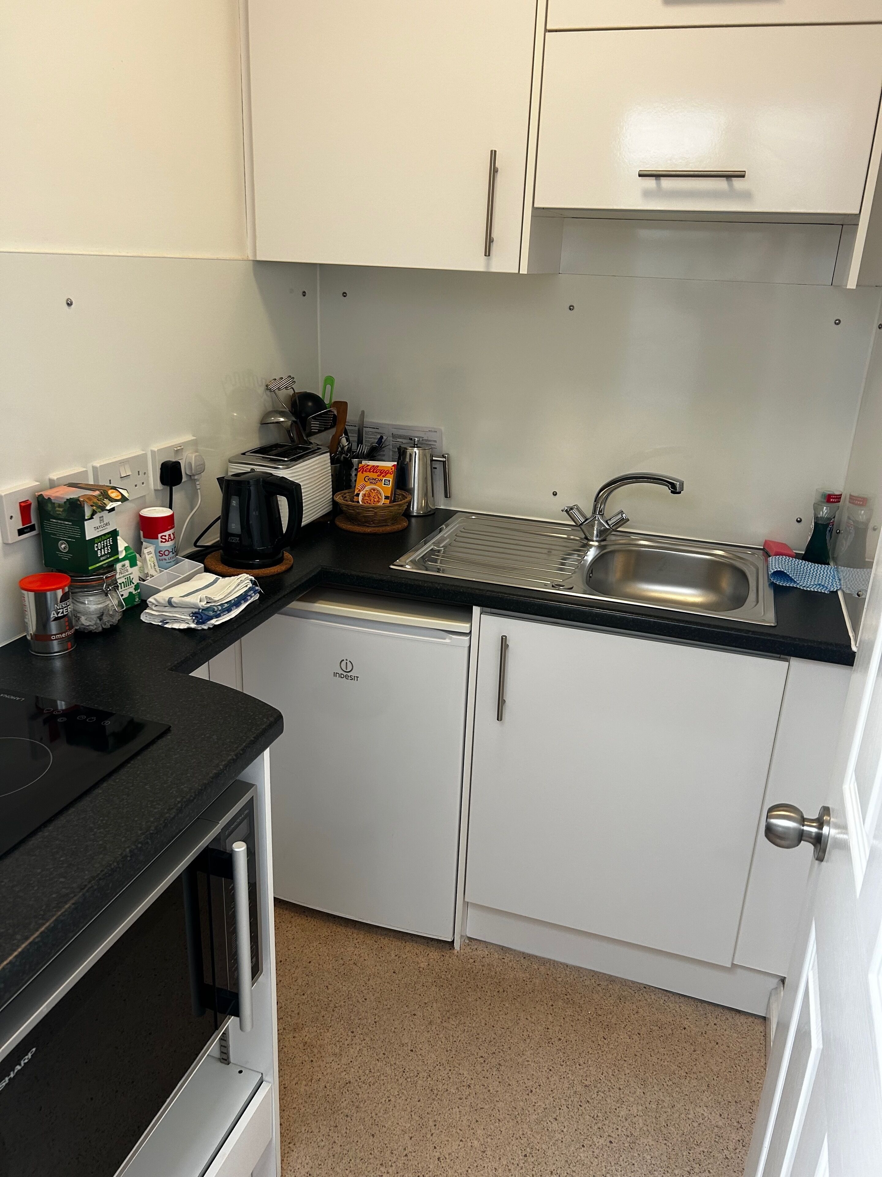A compact kitchen with white cabinets, a black countertop, a built-in dishwasher, and a sink.