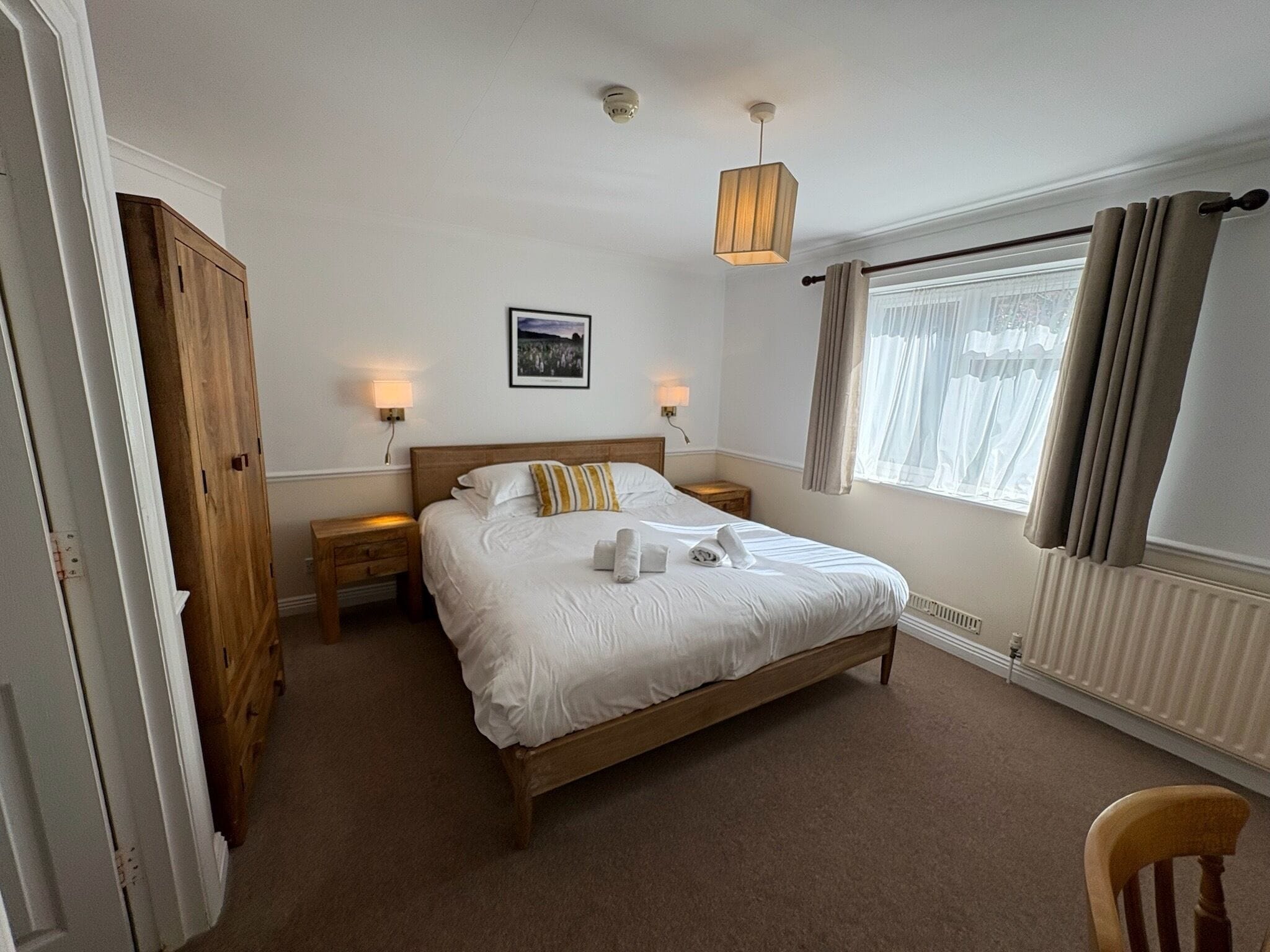 A bedroom with a wooden bed, two bedside lamps, a radiator, and a window with curtains.