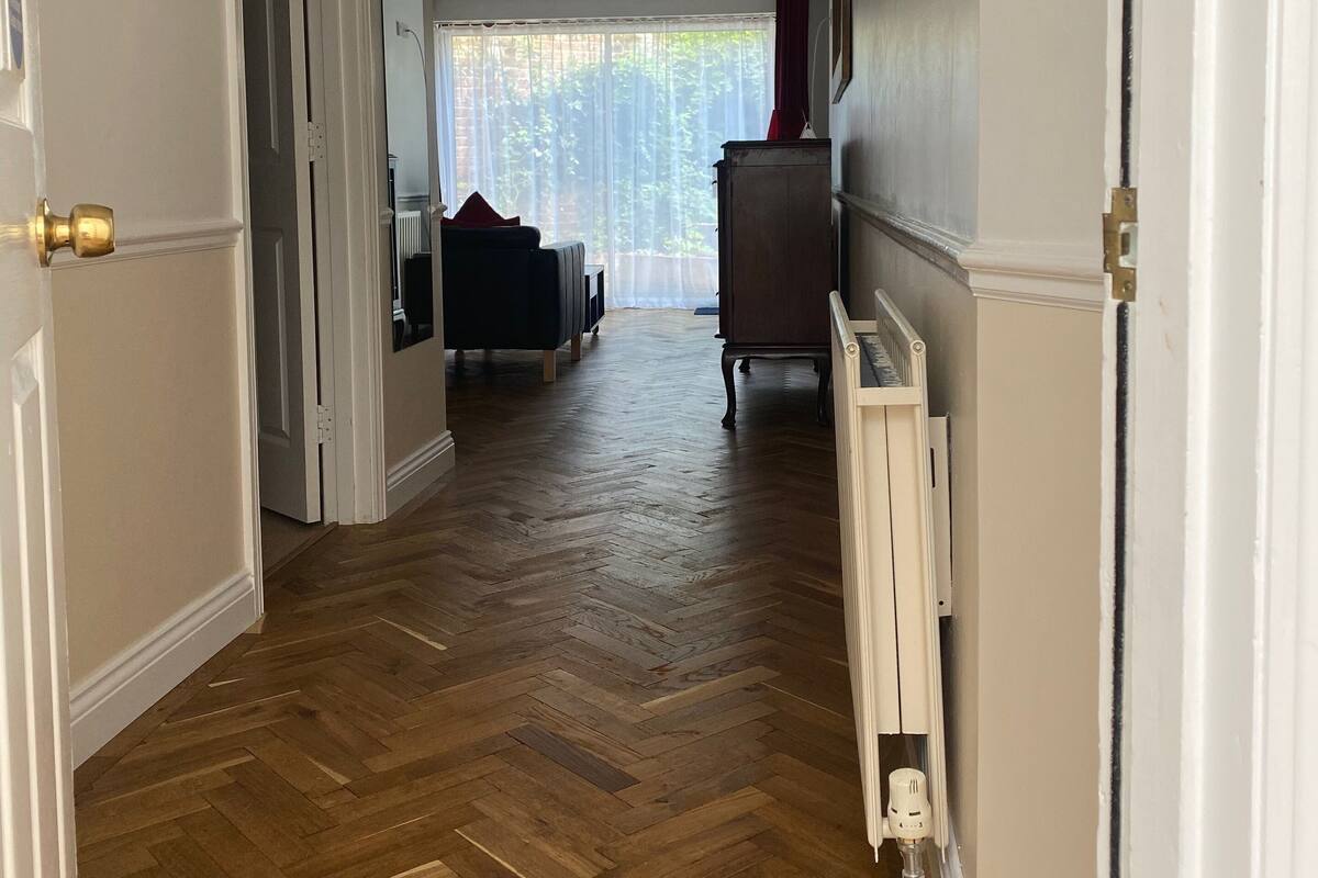 A hallway with wooden flooring, white walls, and a radiator on the right.