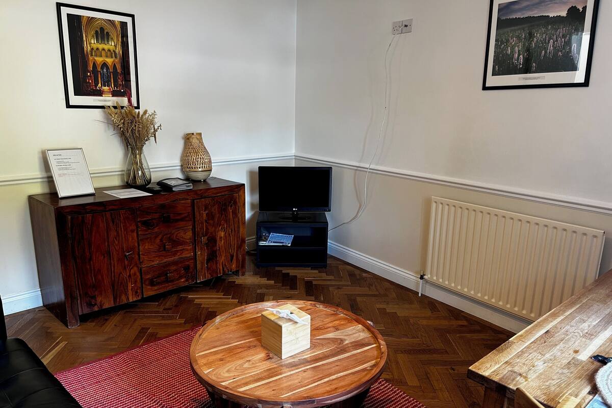 A living room with a wooden cabinet, a television, a round wooden coffee table, and a red rug.