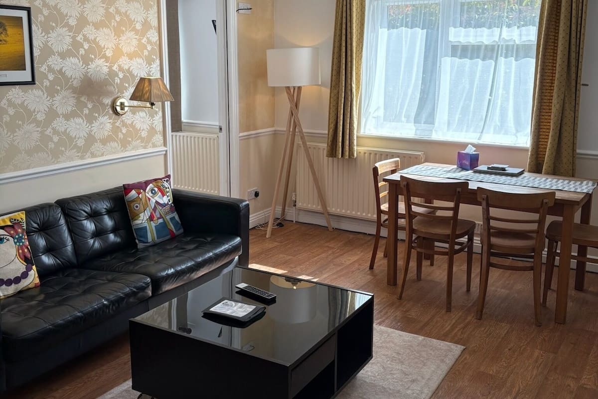 A living room with a sofa, coffee table, lamp, dining table, chairs, and a window with curtains.