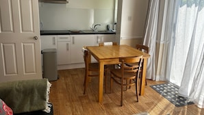 A compact kitchen with white cabinets, a wooden dining table, and a black countertop. - Byways Apartments (Salisbury)