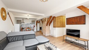 A modern living room with a grey sectional sofa, a wooden TV stand, and a kitchen in the background. - Les Portes de Castelnau - A haven of peace (Castelnau de Montmiral)