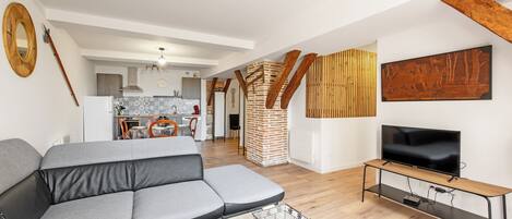 Een moderne woonkamer met een grijze hoekbank, een houten tv-meubel en een keuken op de achtergrond.