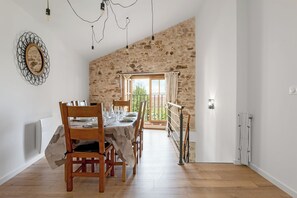 Zona de menjador amb una paret de pedra rústica, taula de fusta preparada per a quatre persones i vista a vegetació a l'exterior.