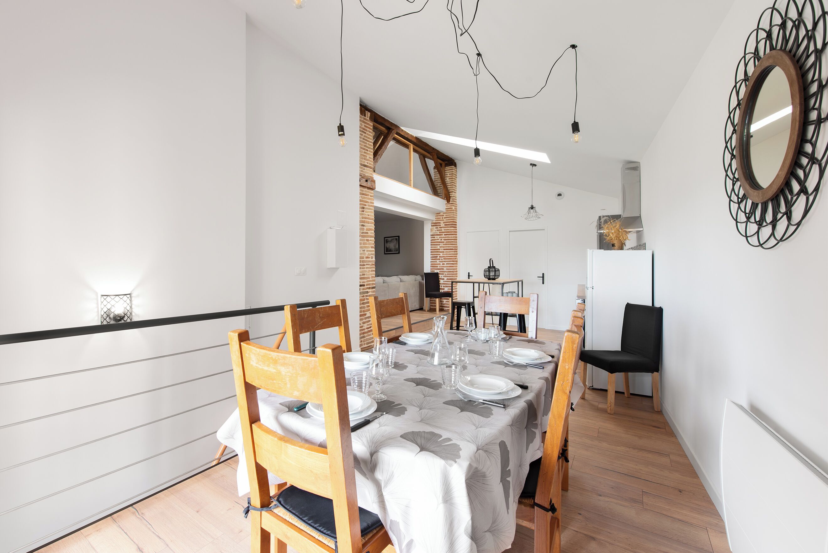 A dining area with a table set for four, wooden chairs, a white tablecloth, and a modern pendant light.