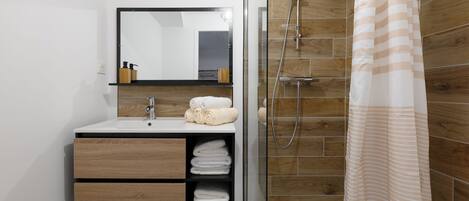 Une salle de bain moderne avec une douche à parois de verre, un meuble-lavabo en bois avec un miroir et des serviettes soigneusement pliées.