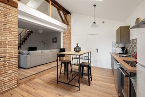 Une cuisine moderne avec un plan de travail en bois, une table à manger avec deux tabourets et un mur en briques.