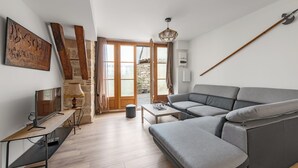 A modern living room with a grey sectional sofa, a wooden coffee table, a TV on a stand, and a stone wall. - Les Portes de Castelnau - A haven of peace (Castelnau de Montmiral)
