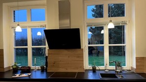 A modern kitchen with a black countertop, two windows, and pendant lights. - Landhaus Baumberge - Cozy vacation home & sauna (Billerbeck)