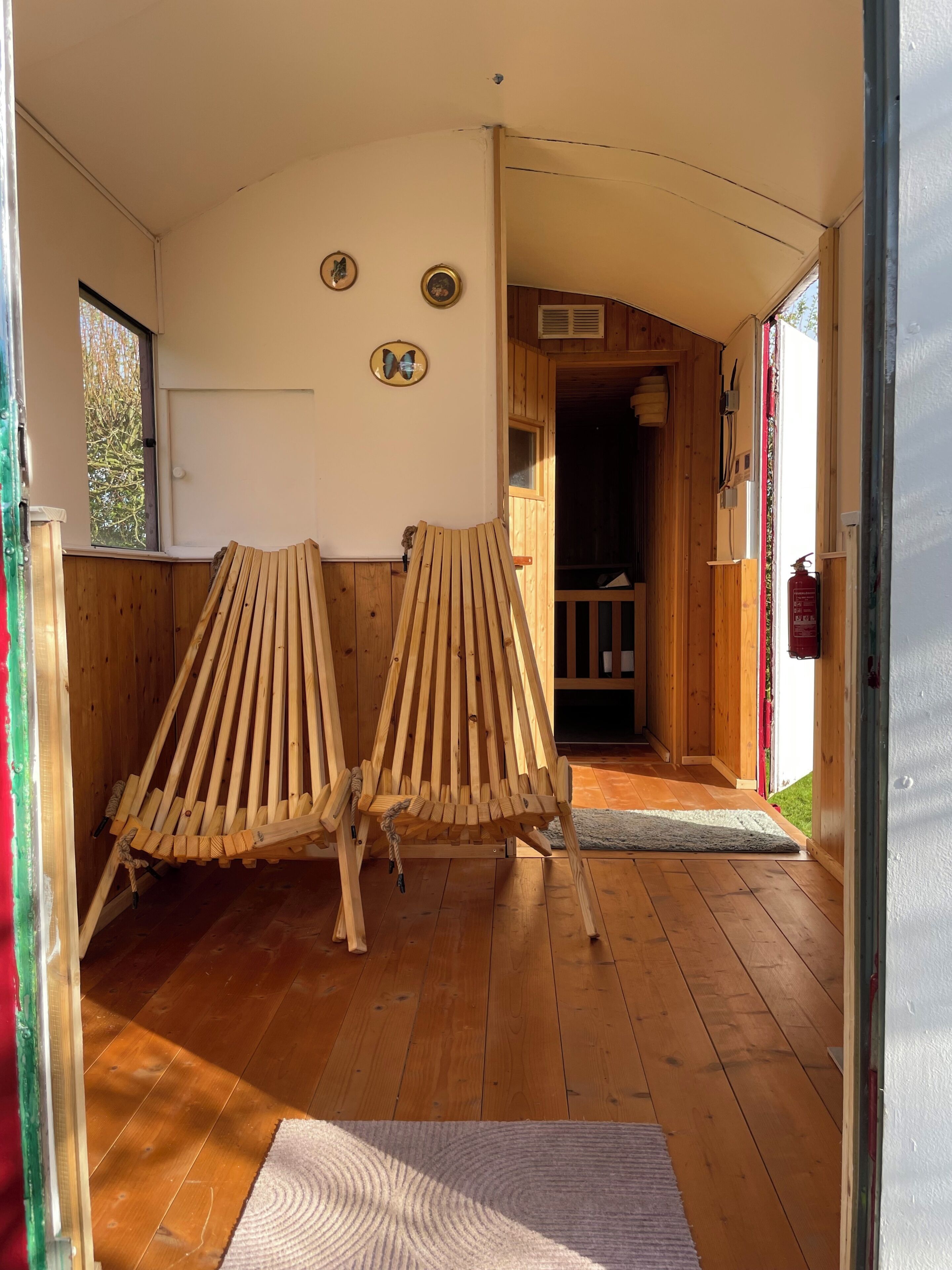 Un intérieur en bois avec deux chaises à lattes, un plancher en bois et une porte donnant sur un espace extérieur.