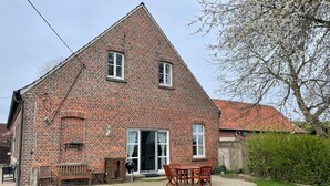 A brick house with a triangular roof, a front door, and a patio with outdoor furniture. - Landhaus Baumberge - Cozy vacation home & sauna (Billerbeck)