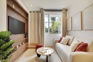 A modern living room with a flat-screen TV, a sofa, a coffee table, and a large window with curtains. - Amazing 2-bedroom apartment with AC in lively Paris (Paris)