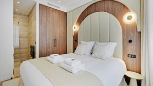 Camera d'albergo moderna con un ampio letto, asciugamani piegati con cura, un armadio in legno e un originale design della parete ad arco.