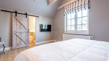 A bedroom with a large bed, a sliding barn door, a television, and a window with curtains.