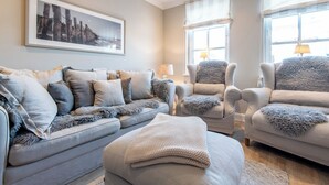 A living room with a grey sofa set, a large framed picture on the wall, and two lamps on the windowsill. - House SyltZauber - Sylt (Sylt)