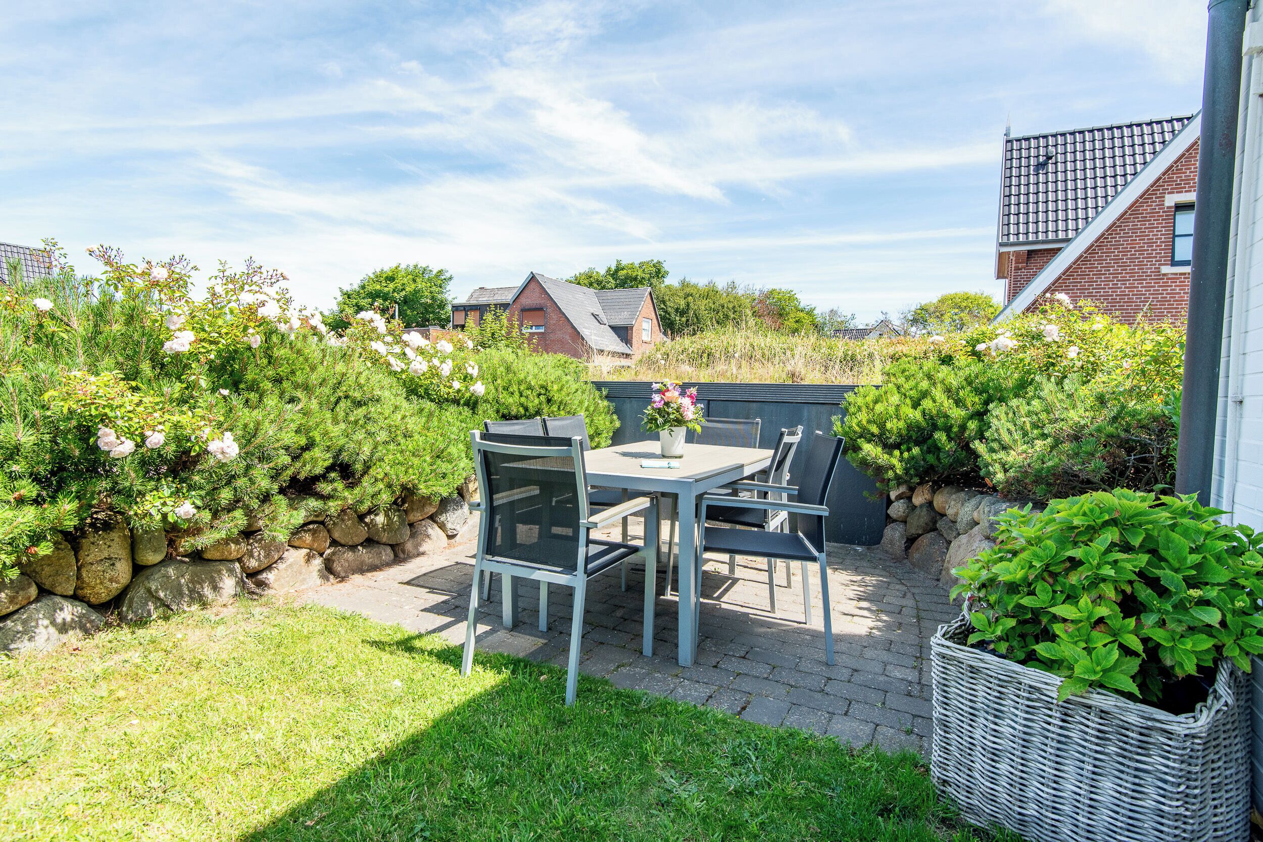 A patio with a table and chairs, surrounded by greenery and a stone wall.