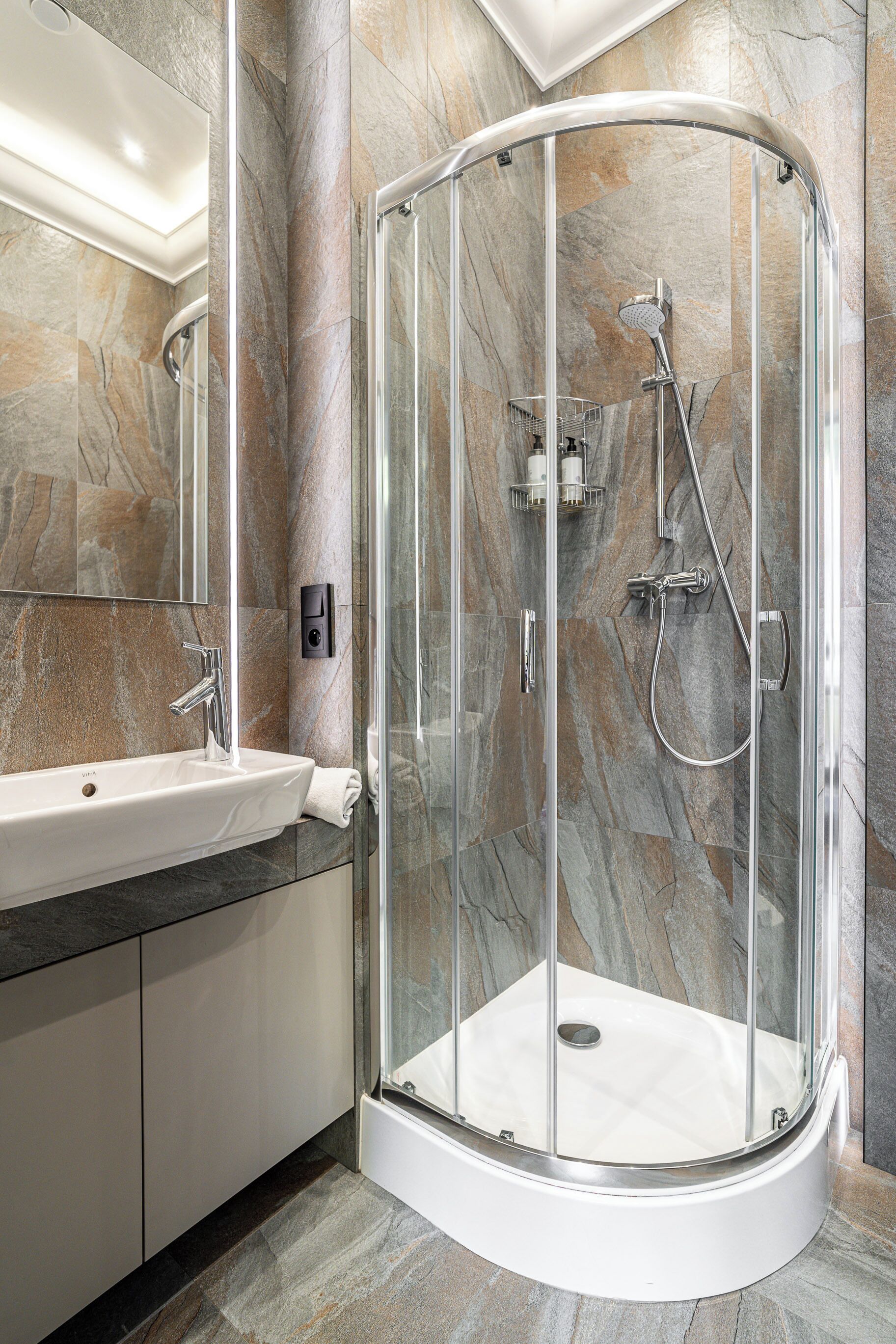 Une salle de bain moderne avec une douche en verre, un lavabo blanc et des murs en marbre.