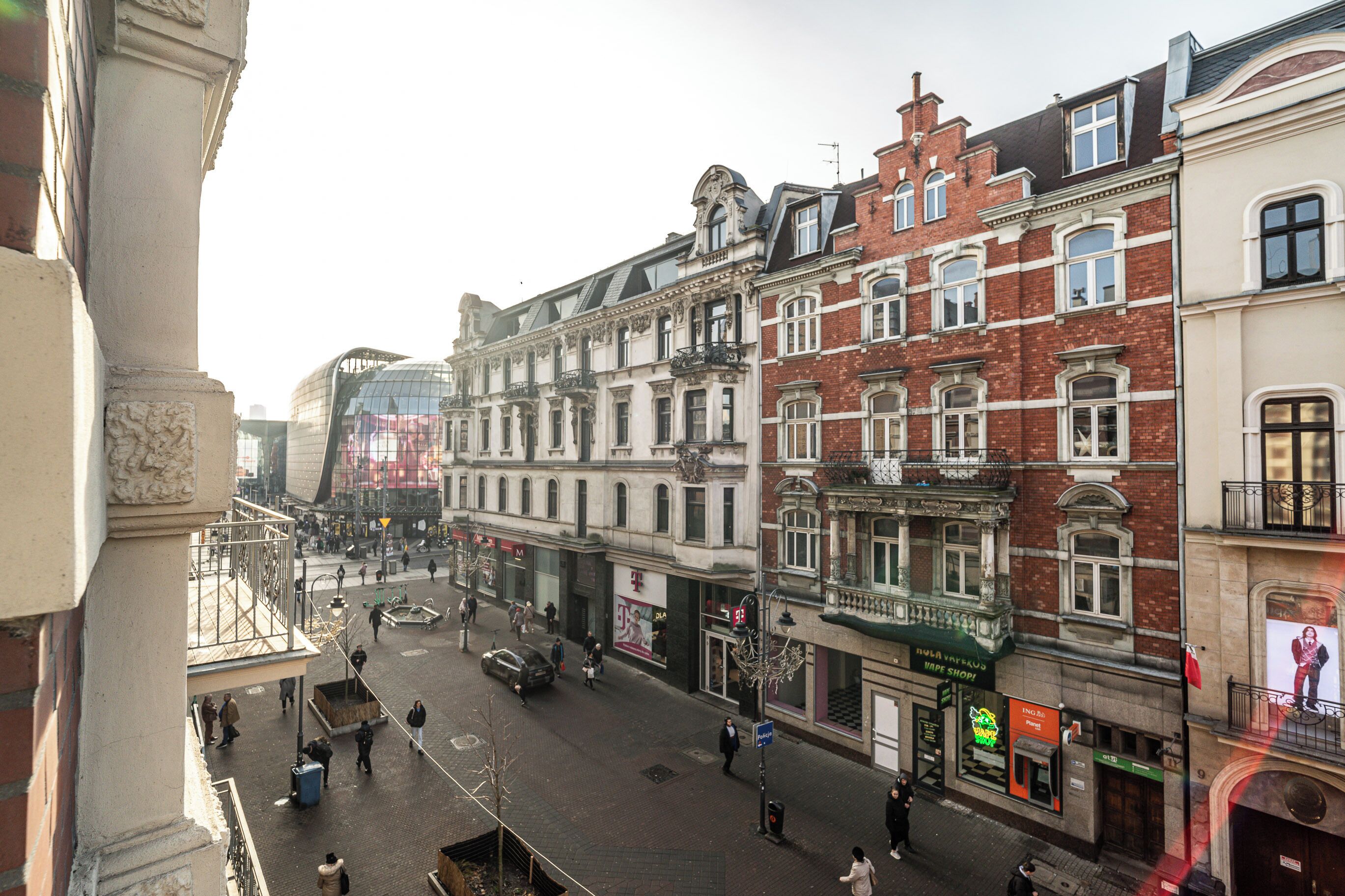 A street view of a European city with historic buildings, a clear sky, and pedestrians.