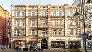 A multi-story building with a brick facade, storefronts, and a sign for 'Policja'. - RentPlanet - Apartamenty Stawowa (Katowice)