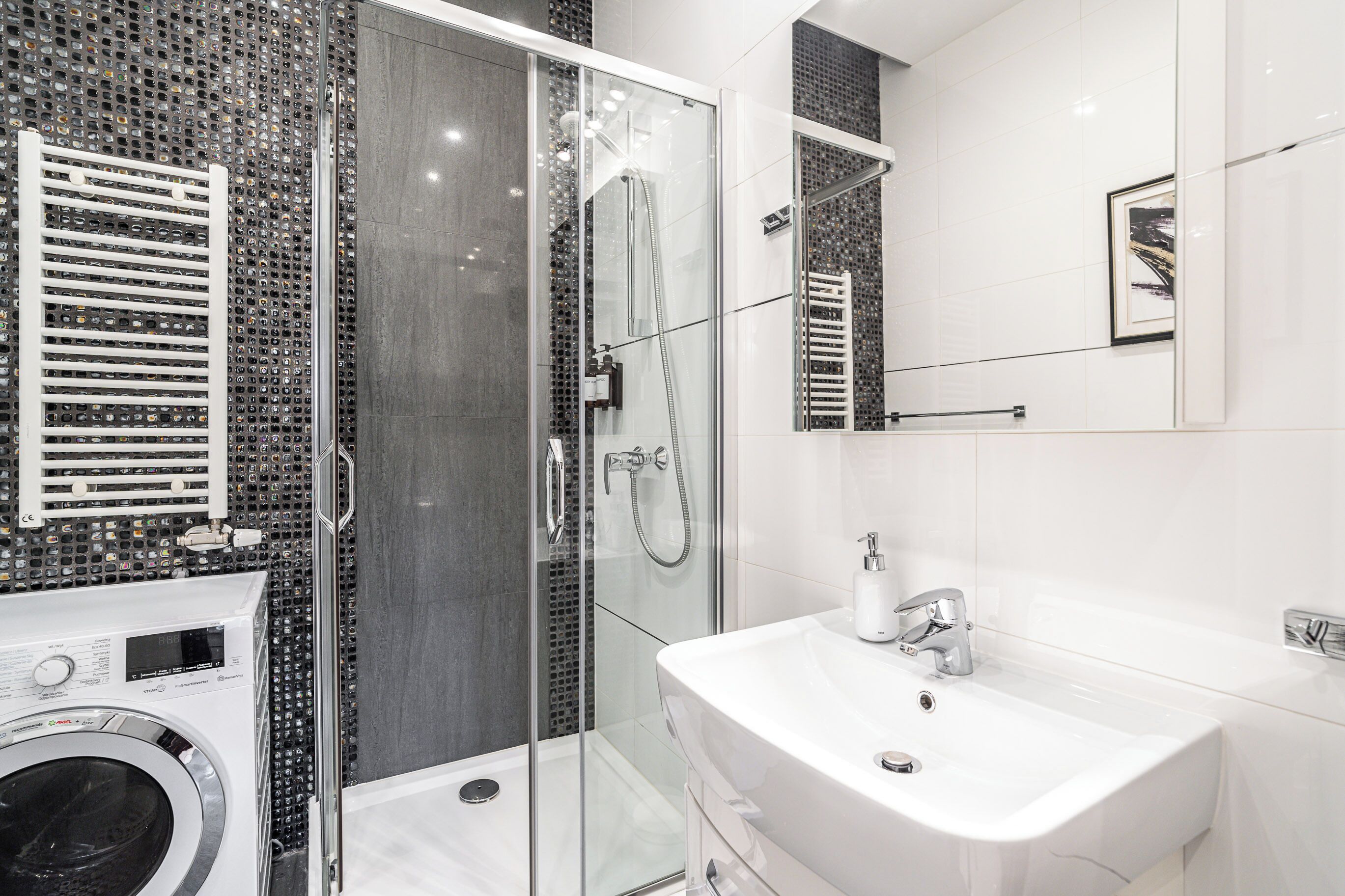 Un baño moderno con ducha envuelta en vidrio, lavadora integrada y un espejo grande.