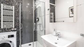 Un baño moderno con ducha envuelta en vidrio, lavadora integrada y un espejo grande.
