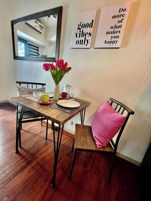 A dining area with a wooden table, chairs, a vase of red tulips, and two motivational posters on the wall. - Shore 3 Comfy & Cozy 1BR unit near MOA (Pasay City)