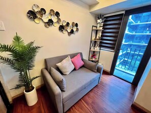 Ein Wohnzimmer mit grauem Sofa, einer Topfpflanze und einem Wanddekor.