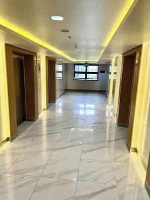 A corridor with marble flooring, recessed lighting, and doors on both sides. - Shore 3 Comfy & Cozy 1BR unit near MOA (Pasay City)