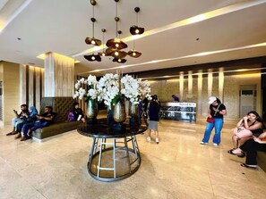 A lobby with a round table surrounded by vases of white flowers, a reception desk, and people sitting and standing. - Shore 3 Comfy & Cozy 1BR unit near MOA (Pasay City)