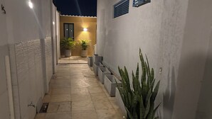Un pasillo estrecho con suelo de baldosas, plantas en macetas y una puerta al final.