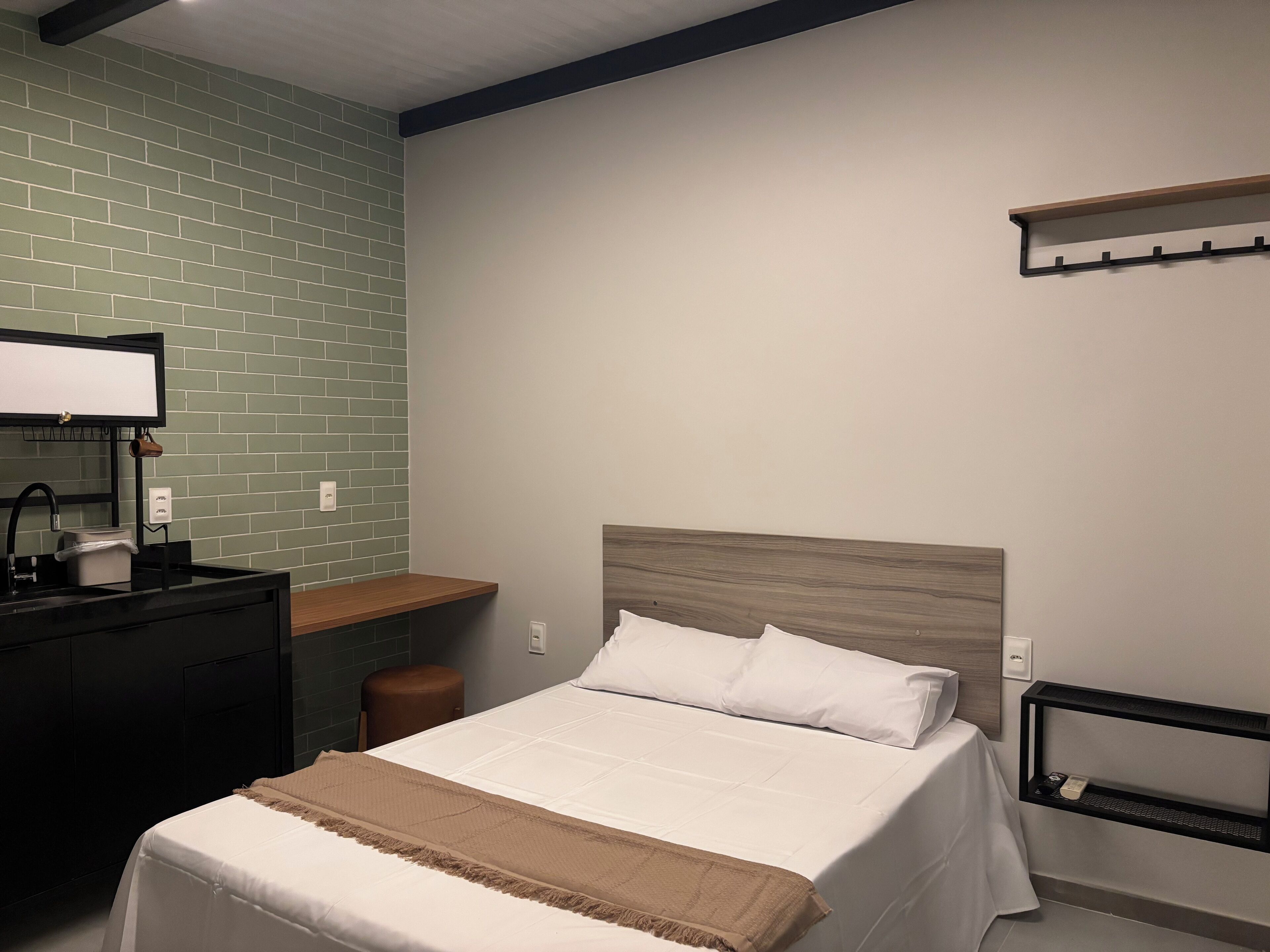 Een netjes ingerichte hotelkamer met een bed, een bureau, een klein krukje en een wandplank.