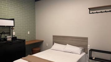 Een netjes ingerichte hotelkamer met een bed, een bureau, een klein krukje en een wandplank.