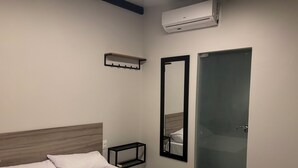 Una habitación de hotel con cama, mesita de noche, espejo y aire acondicionado.