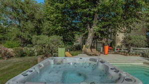 A hot tub in a backyard with a pool, surrounded by trees and a wooden deck.