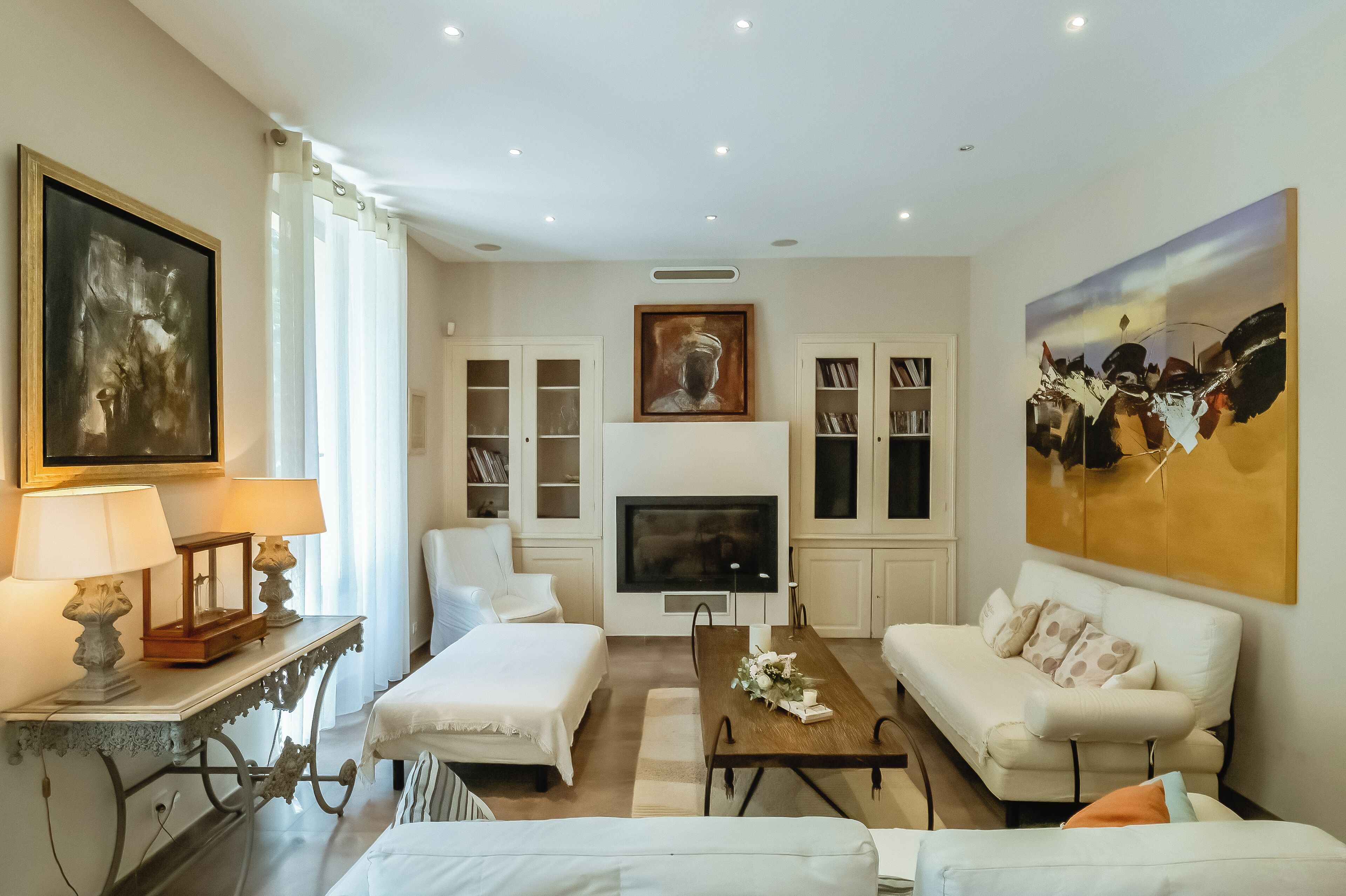 A modern living room with a fireplace, white furniture, and artwork on the walls.
