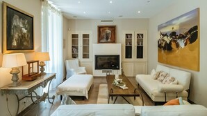 A modern living room with a fireplace, white furniture, and artwork on the walls.