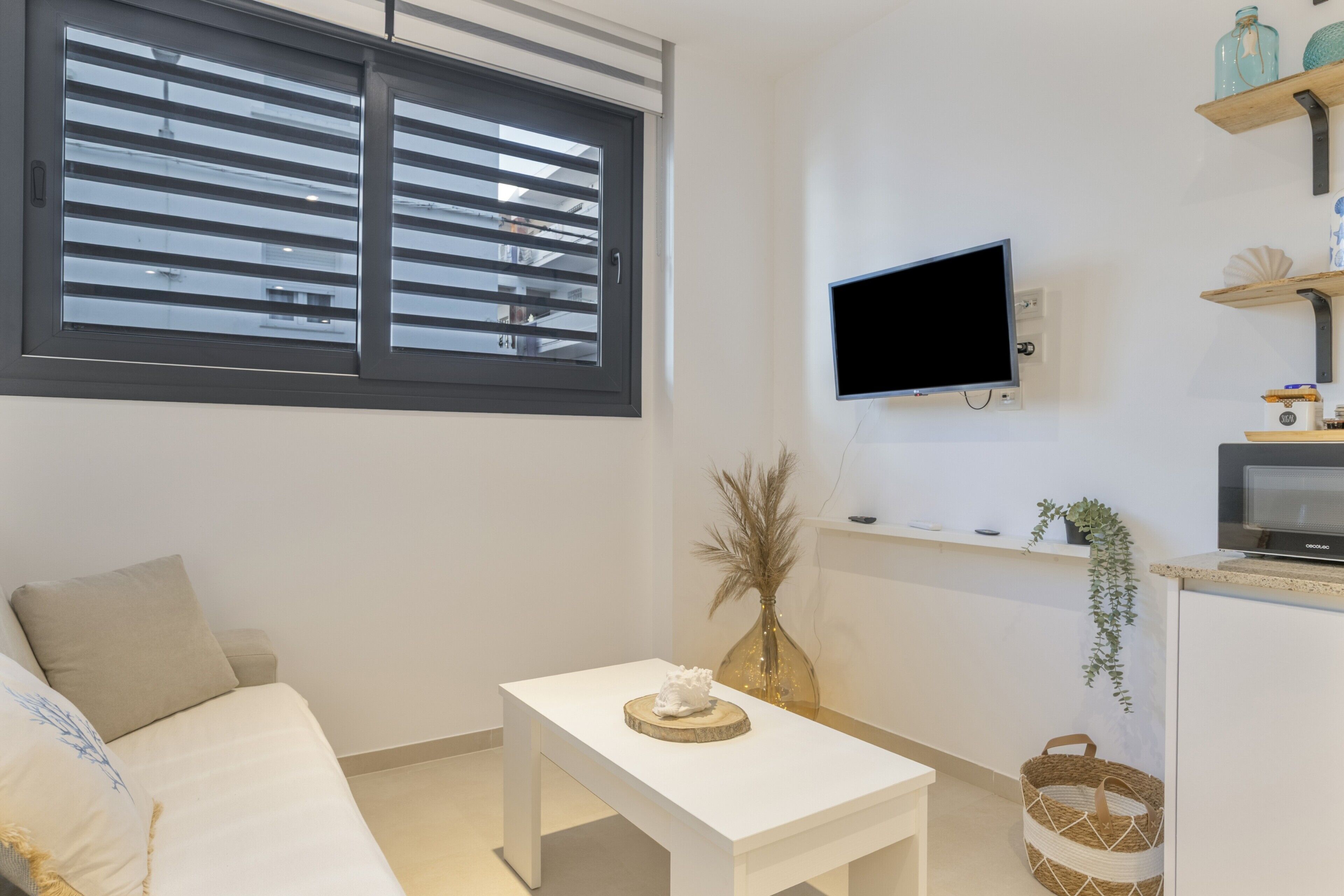 Een moderne kamer met een bed, een klein tafeltje, een aan de muur bevestigde televisie en een raam met zonwering.