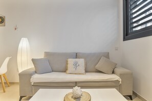 A neutral-toned living room with a sofa, a decorative pillow, a white table, and a wall-mounted light fixture. - Comfortable "Tarifa Dreams" Studio, Excellent Location. Perfect for Couples (Tarifa)