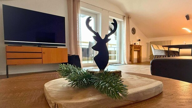 A modern living room with a wooden coffee table, a decorative antler sculpture, and a television in the background. - Aloisius | Balcony Apt · Workation · Königscard (Nesselwang)