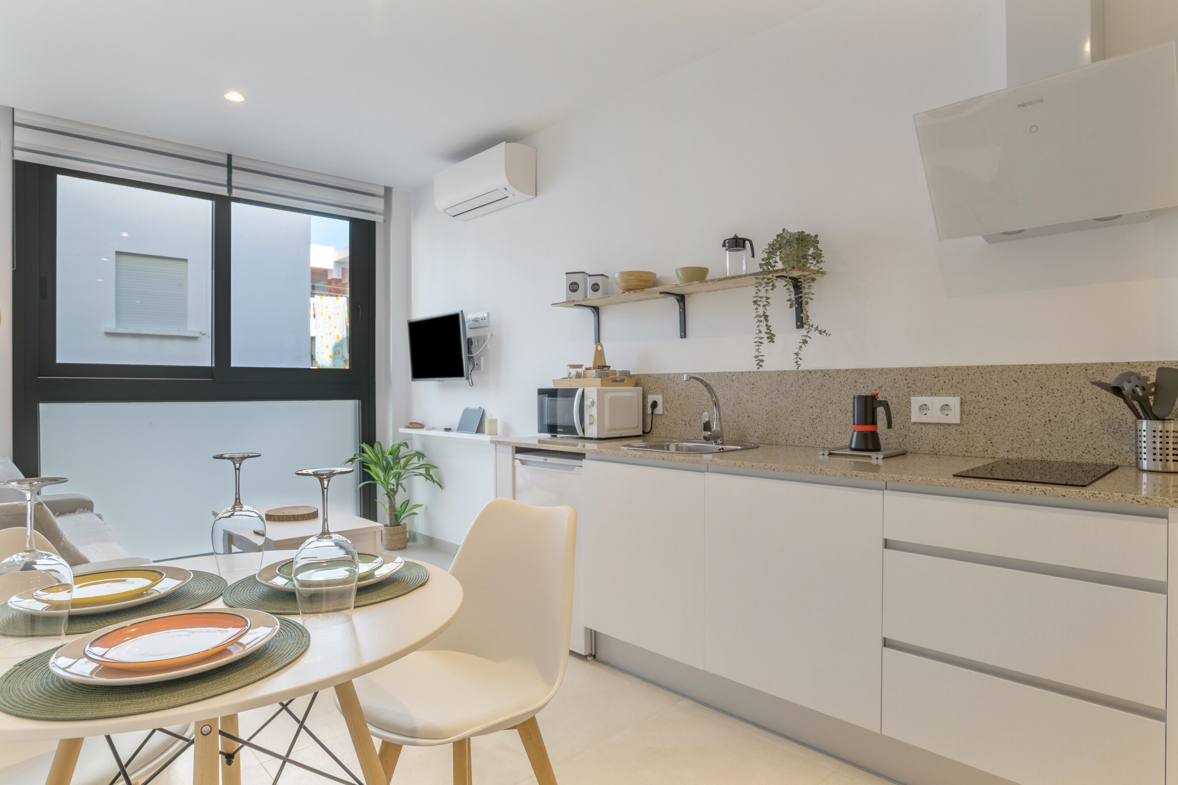 A modern kitchen with a dining table set for four, a microwave, a coffee maker, and a plant on the counter.