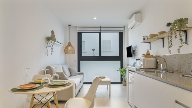 A modern kitchen with a dining area, a sofa, and a TV.