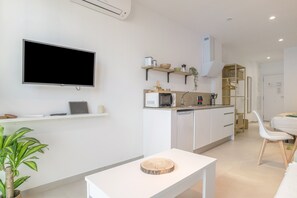A modern kitchen with a flat-screen TV, white cabinetry, a dining area with a white table and chair, and a small plant. - Comfortable "Black Palm" Studio, Excellent Location – Perfect for Couples (Tarifa)
